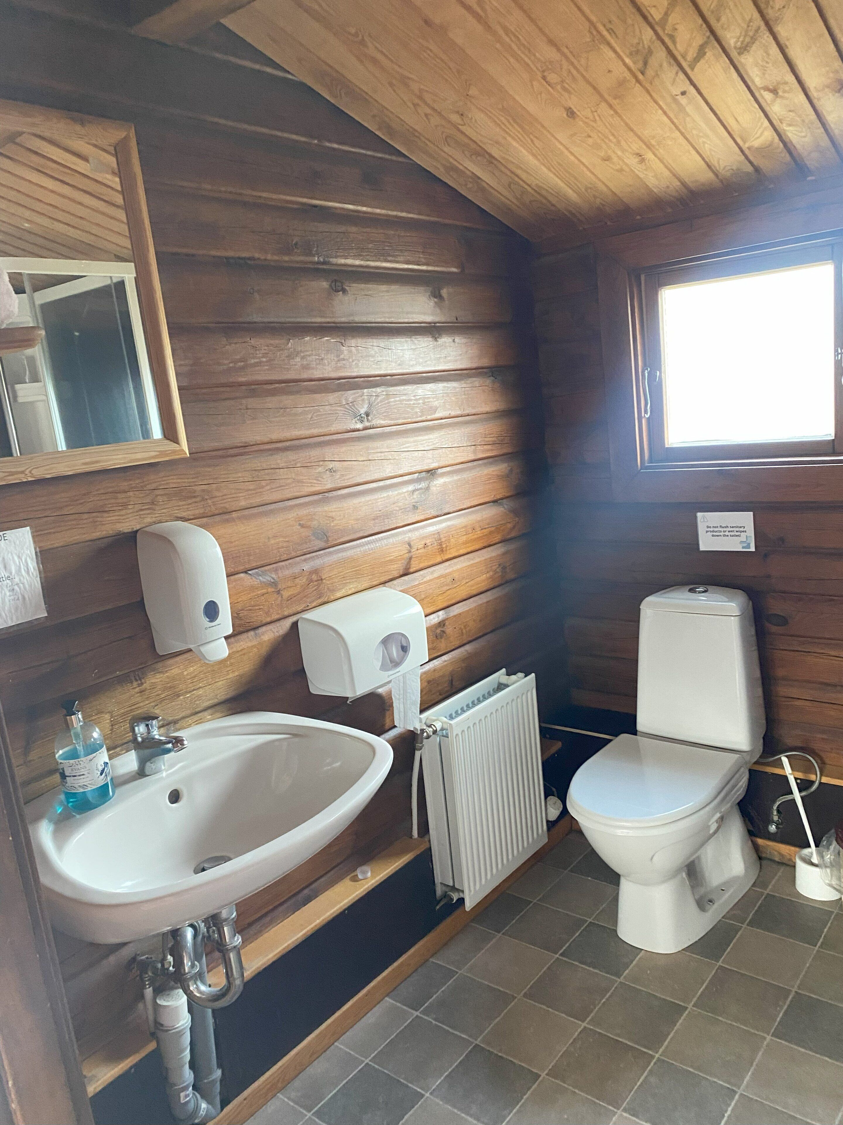 A wooden-paneled bathroom with a sink, toilet, and window.