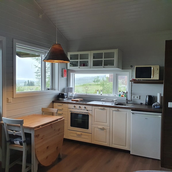 A kitchen with a wooden bench, a stove, a microwave, and a window with a view of greenery.