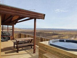 Terraza de madera con jacuzzi y una mesa, con vistas a un paisaje extenso.