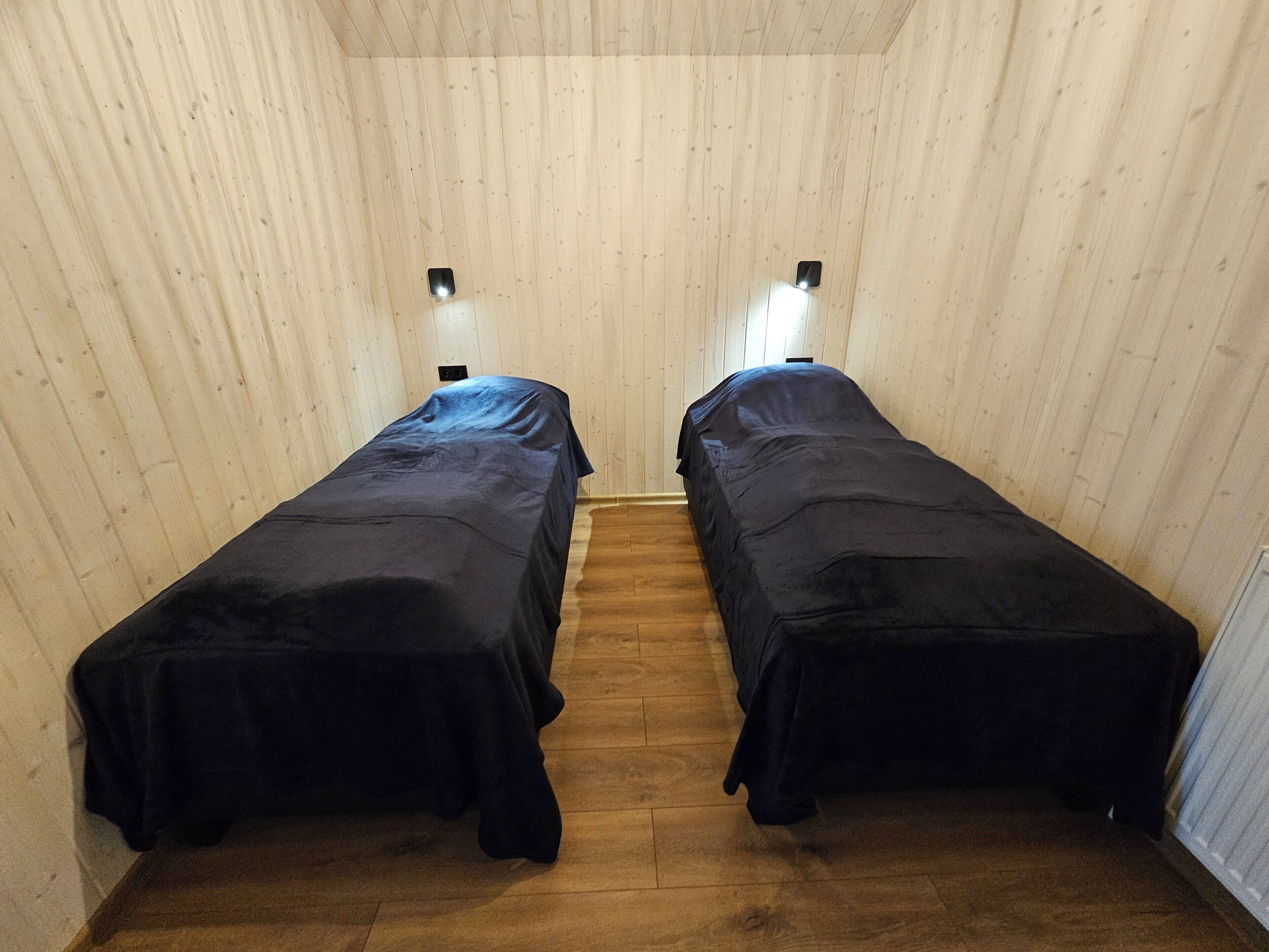 Una habitación con dos camas individuales pegadas a una pared de madera, cada una con una mesita de noche y una lámpara de pared.