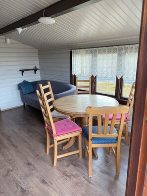 A cozy room with a round wooden table and chairs, a blue sofa, and a wooden bench. - Uthlid Cottages (Bláskógabyggd)