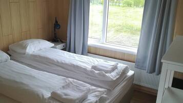 Une chambre avec deux lits, une table de chevet avec une lampe, une fenêtre avec des rideaux et un radiateur.