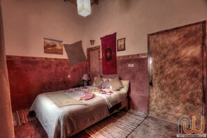 A bedroom with a bed, a door, and a wall with a rug and a picture.