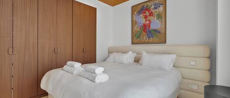 Un dormitorio moderno con una cama grande, un armario de madera y un cuadro abstracto de colores en la pared.