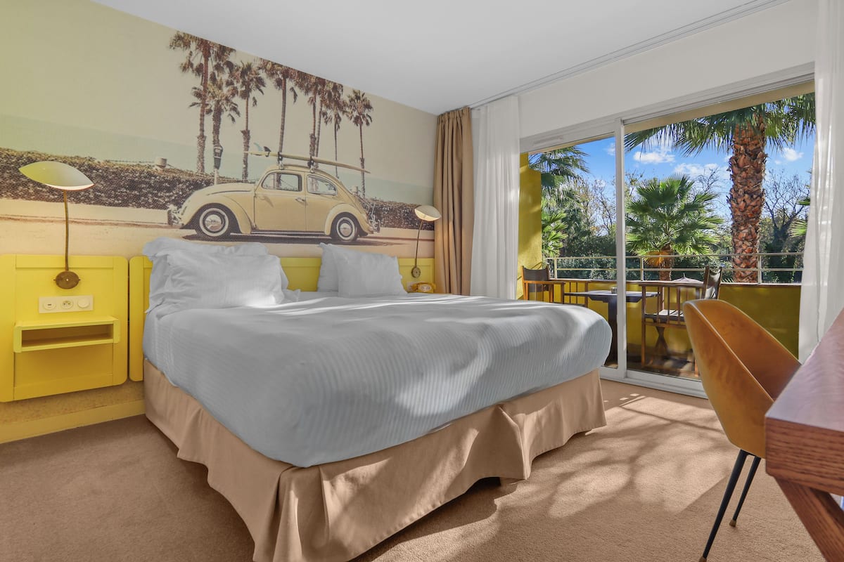 Une chambre à coucher comprenant un lit, une table de chevet, une lampe, une chaise et un balcon avec vue sur les palmiers.