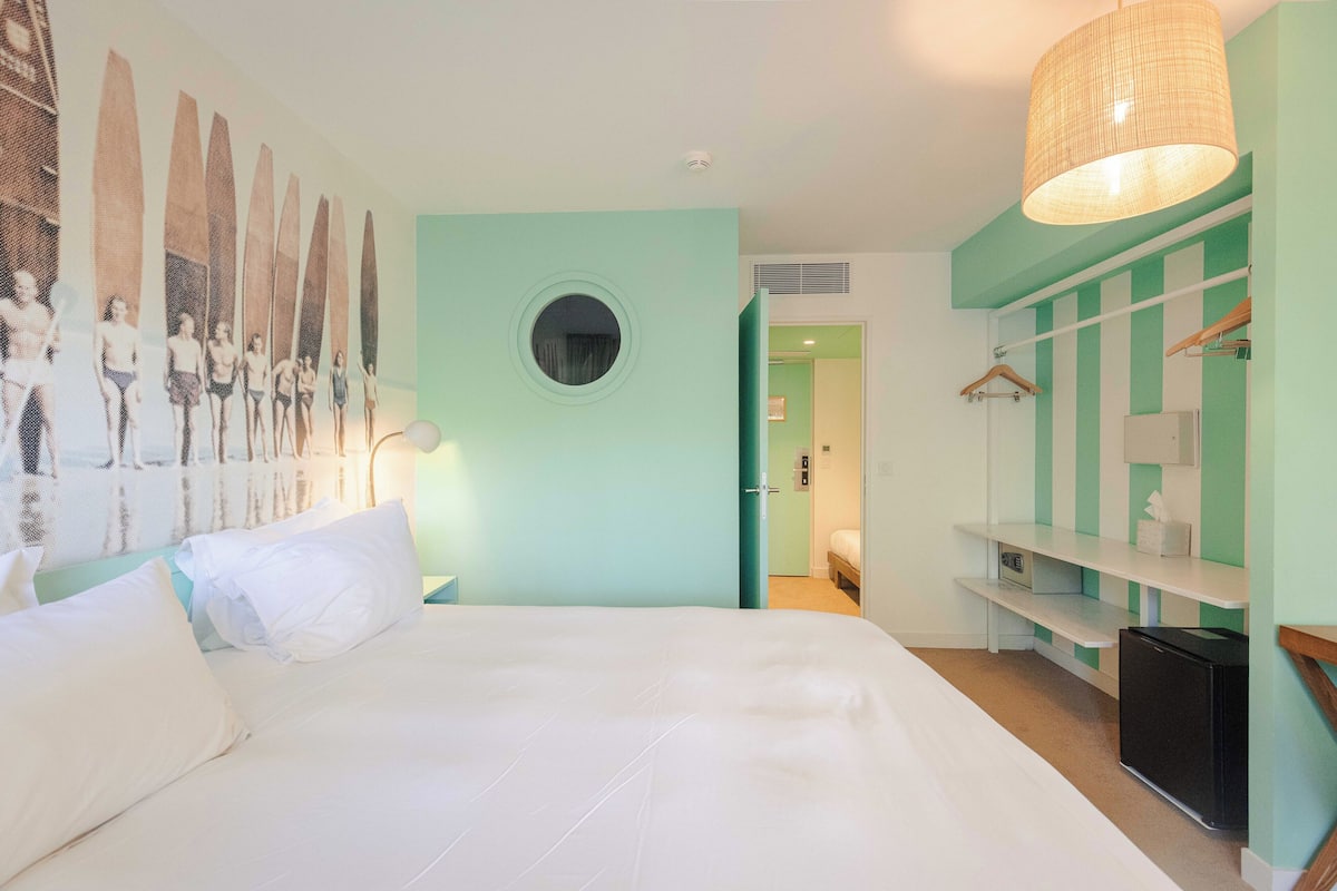 Une chambre à coucher avec un lit, une fenêtre ronde, une armoire et un luminaire suspendu.