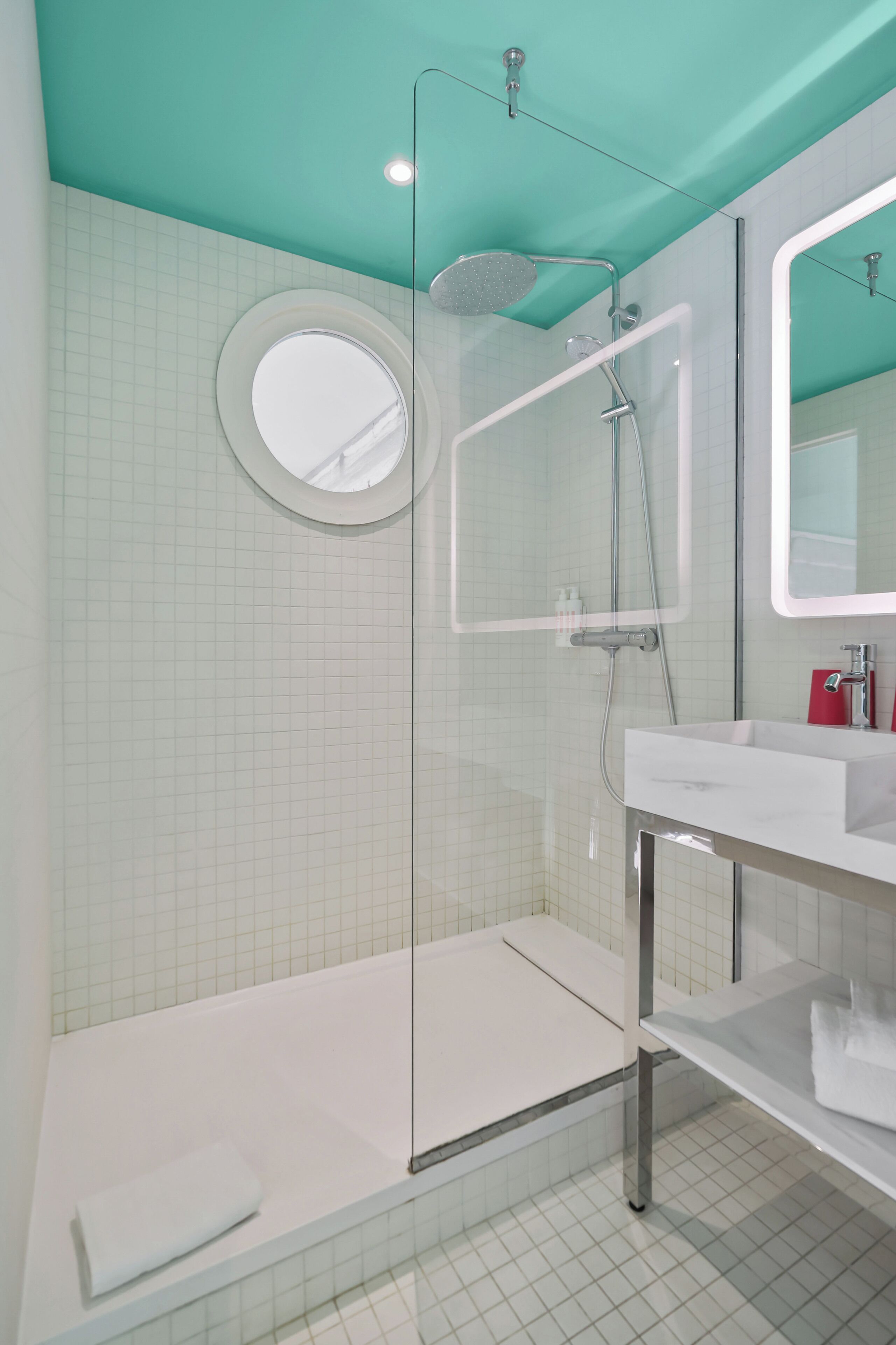 Une salle de bain moderne avec une douche à parois de verre, un miroir rond et un lavabo blanc.