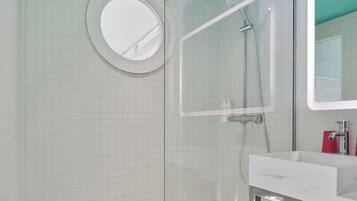 Une salle de bain moderne avec une douche à parois de verre, un miroir rond et un lavabo blanc.