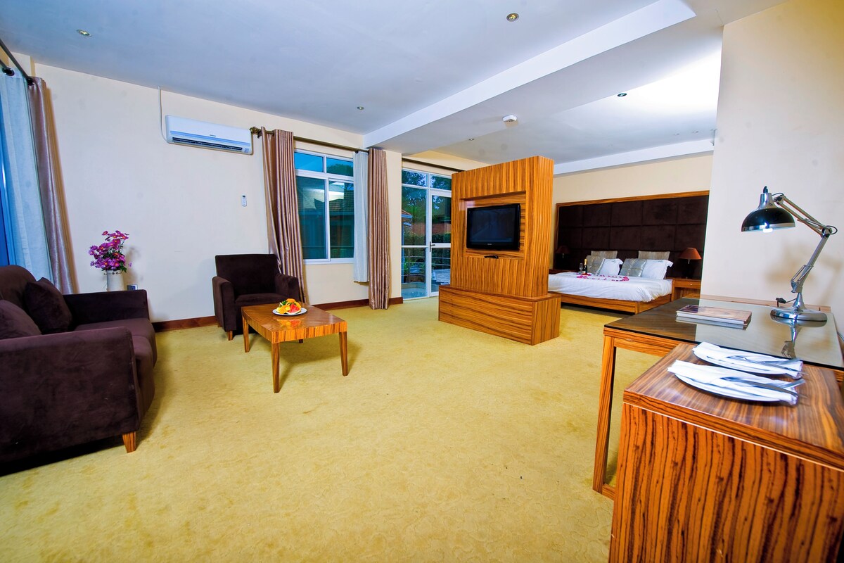 A hotel room with a bed, a TV, a desk, a sofa, and a window with curtains.