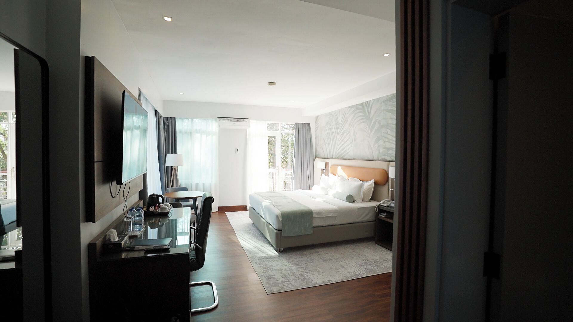 Habitación de hotel con cama, escritorio, silla, televisor y vista al exterior.