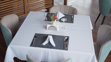 Une table dressée pour deux personnes, avec une nappe blanche, deux chaises, un vase contenant une fleur rouge et une serviette posée sur un set de table.
