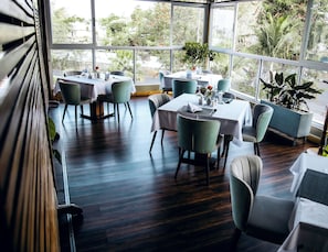 A restaurant with multiple tables and chairs, large windows, and indoor plants. - Urban by CityBlue, Kigali, Rwanda (Kigali)