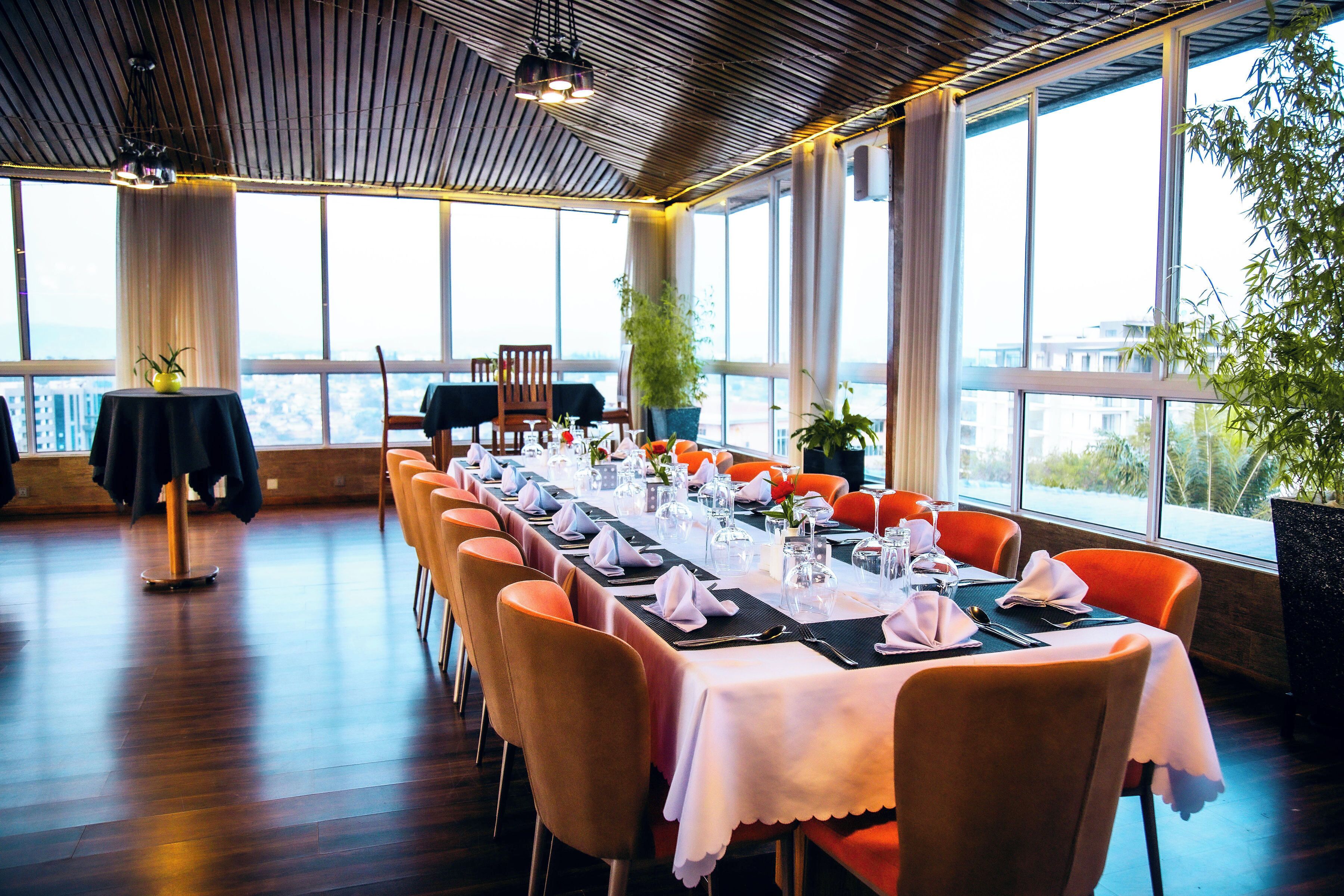 Una larga mesa de comedor dispuesta para una comida, con sillas, ventanas amplias y vistas a la ciudad.
