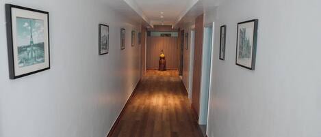 Un pasillo con cuadros en las paredes, piso de madera y un accesorio de iluminación al final.