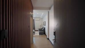 A hallway with a wooden panel wall, a seating area with a sofa and armchairs, and a wall-mounted air conditioning unit. - Urban by CityBlue, Kigali, Rwanda (Kigali)
