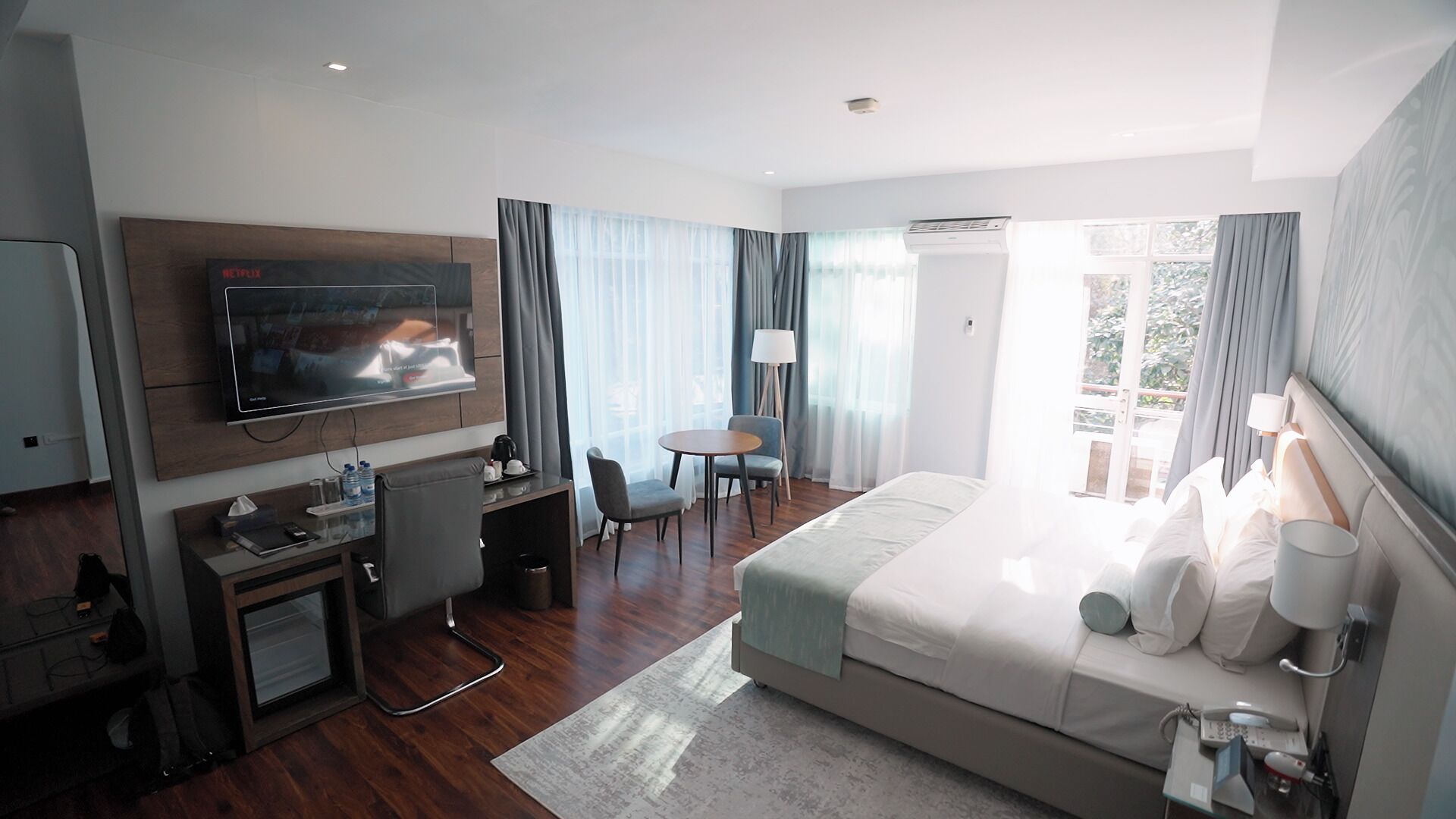 Una habitación de hotel moderna con una cama grande, un escritorio con silla, un televisor y una pequeña mesa con sillas.