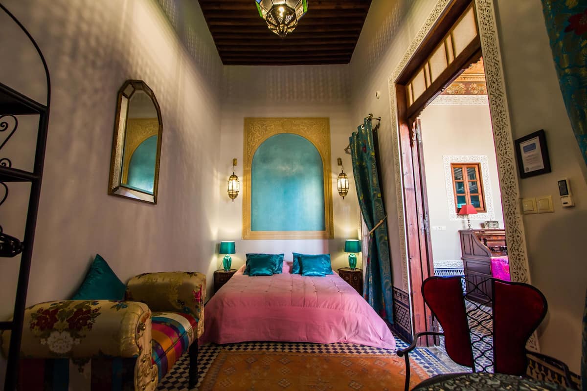 A bedroom with a bed, two bedside tables, a chair, and a decorative mirror.