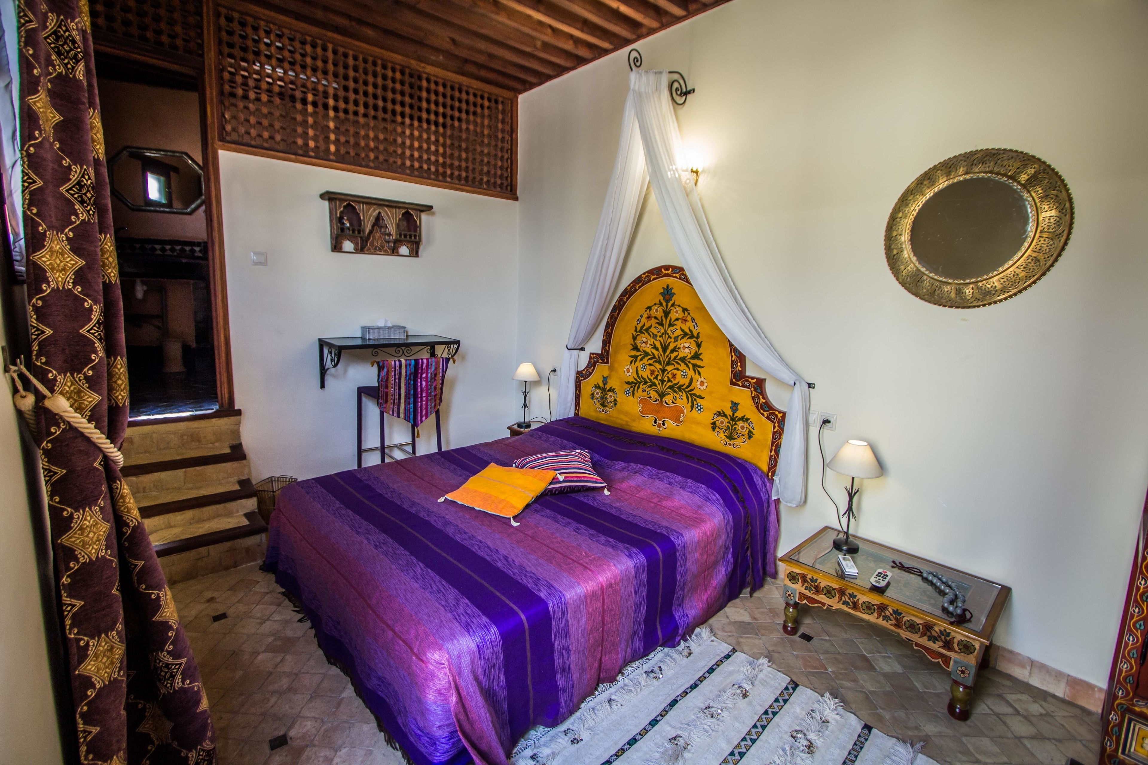 A bedroom with a bed, a nightstand, a mirror, and a staircase.