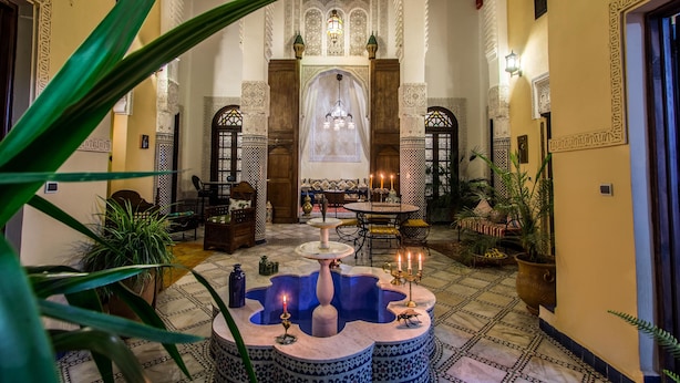 Un interior tradicional marroquí con una fuente, zona de estar y arcos ornamentales.