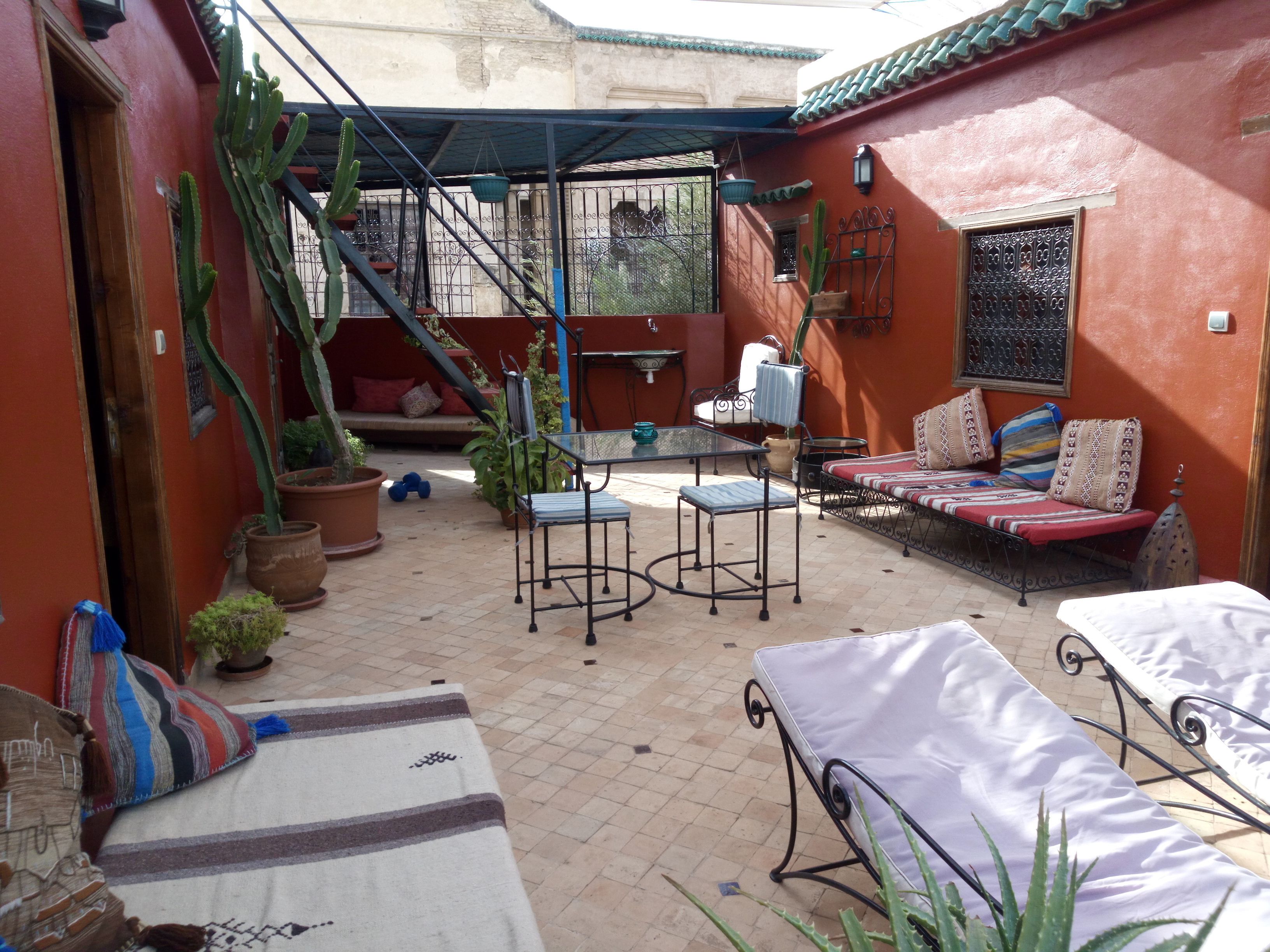 Un patio con sofá, sillas y una mesa. Hay plantas en macetas y una escalera que lleva a un nivel superior.