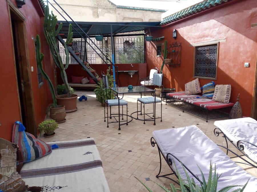 Un patio con sofá, sillas y una mesa. Hay plantas en macetas y una escalera que lleva a un nivel superior.