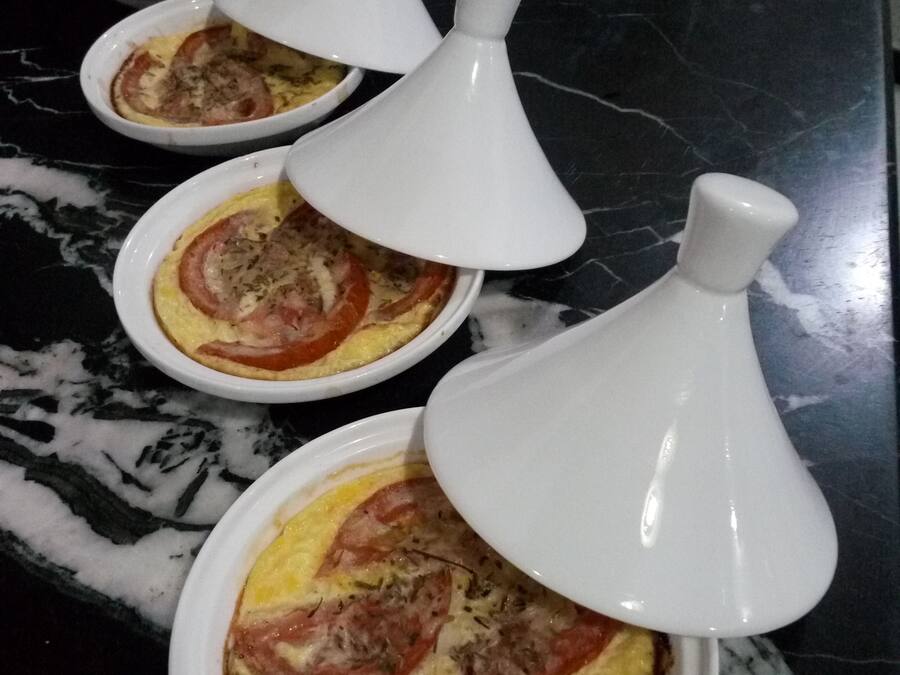 Cuatro recipientes blancos de cerámica con tapas, que contienen comida, sobre una encimera de mármol oscuro.