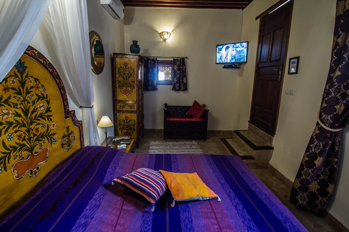 A room with a bed, a television, a window with curtains, and a door.