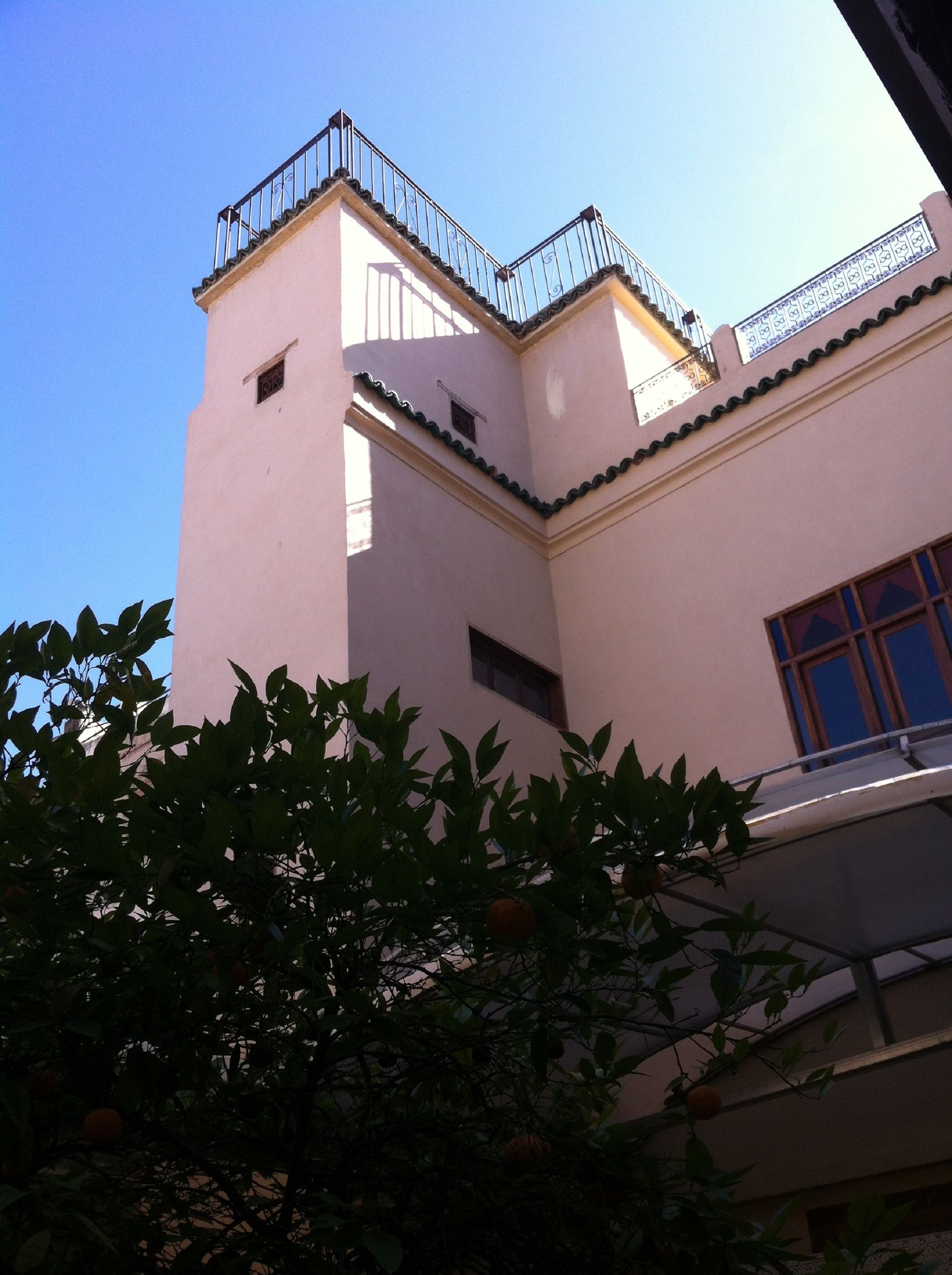Un immeuble à la façade rose, doté d’un balcon avec des balustrades noires et d’une fenêtre au cadre bleu.