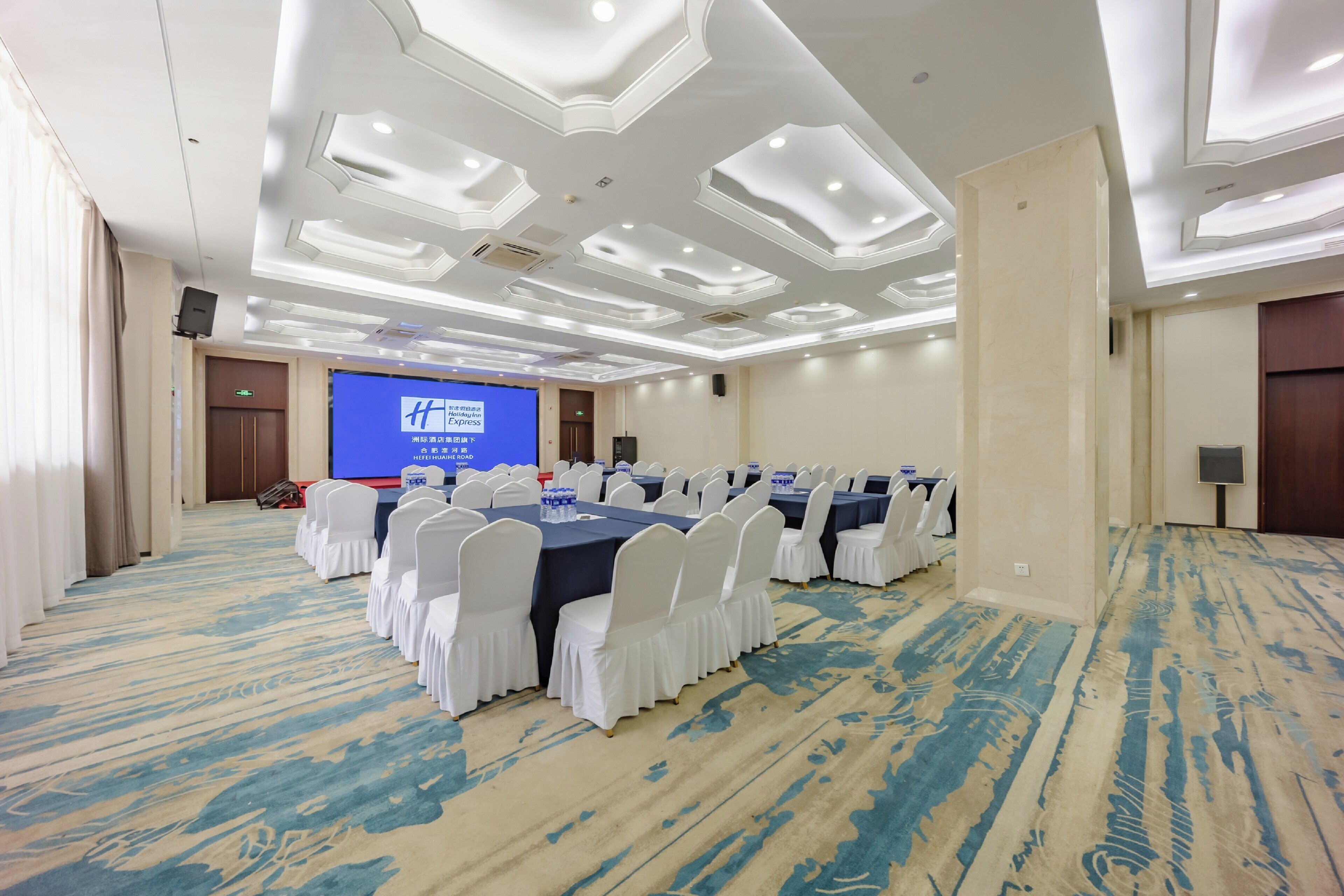 A conference room with a large table, white chairs, and a screen displaying a presentation.
