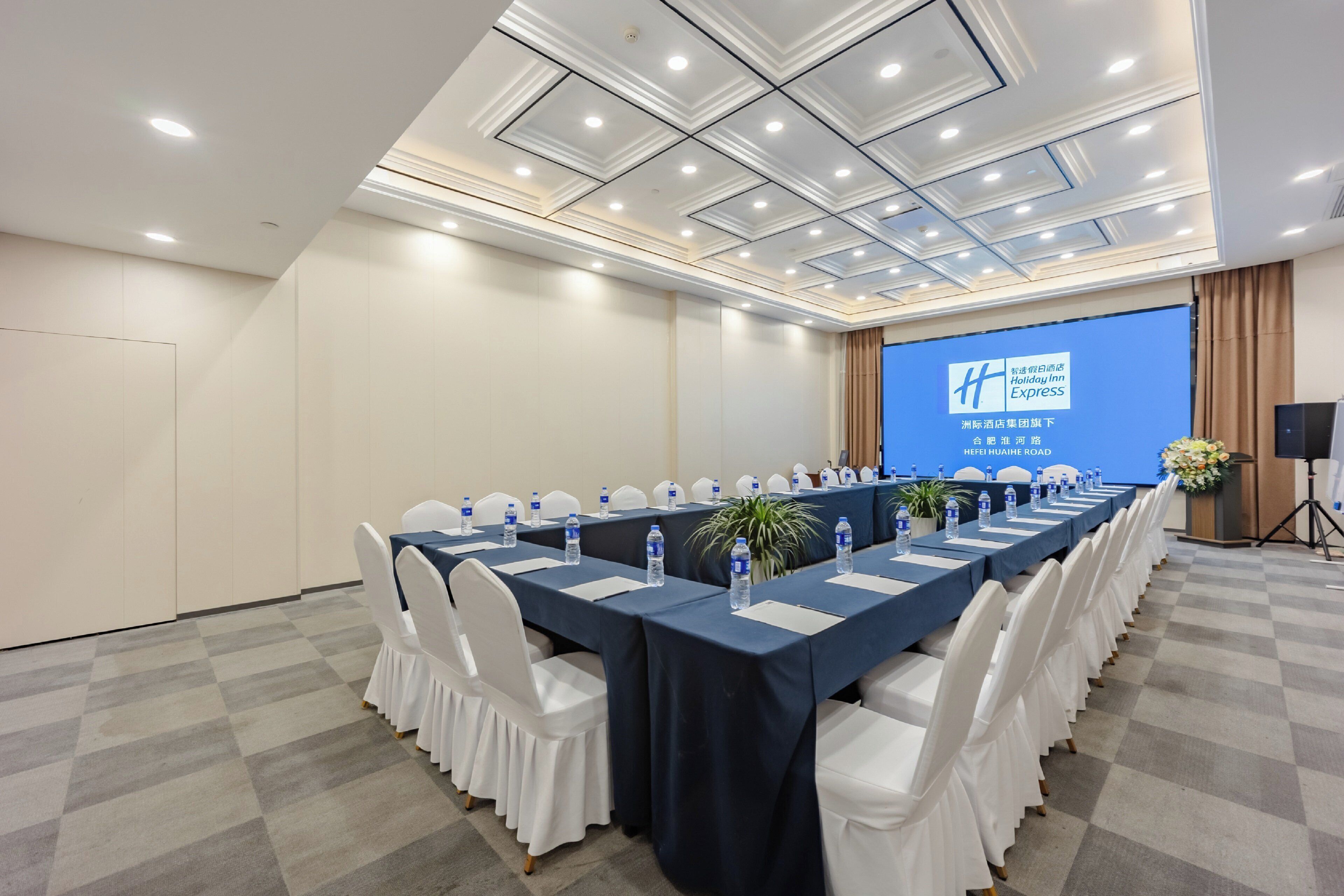 A conference room with a long table, white chairs, and a blue screen displaying the Holiday Inn Express logo.