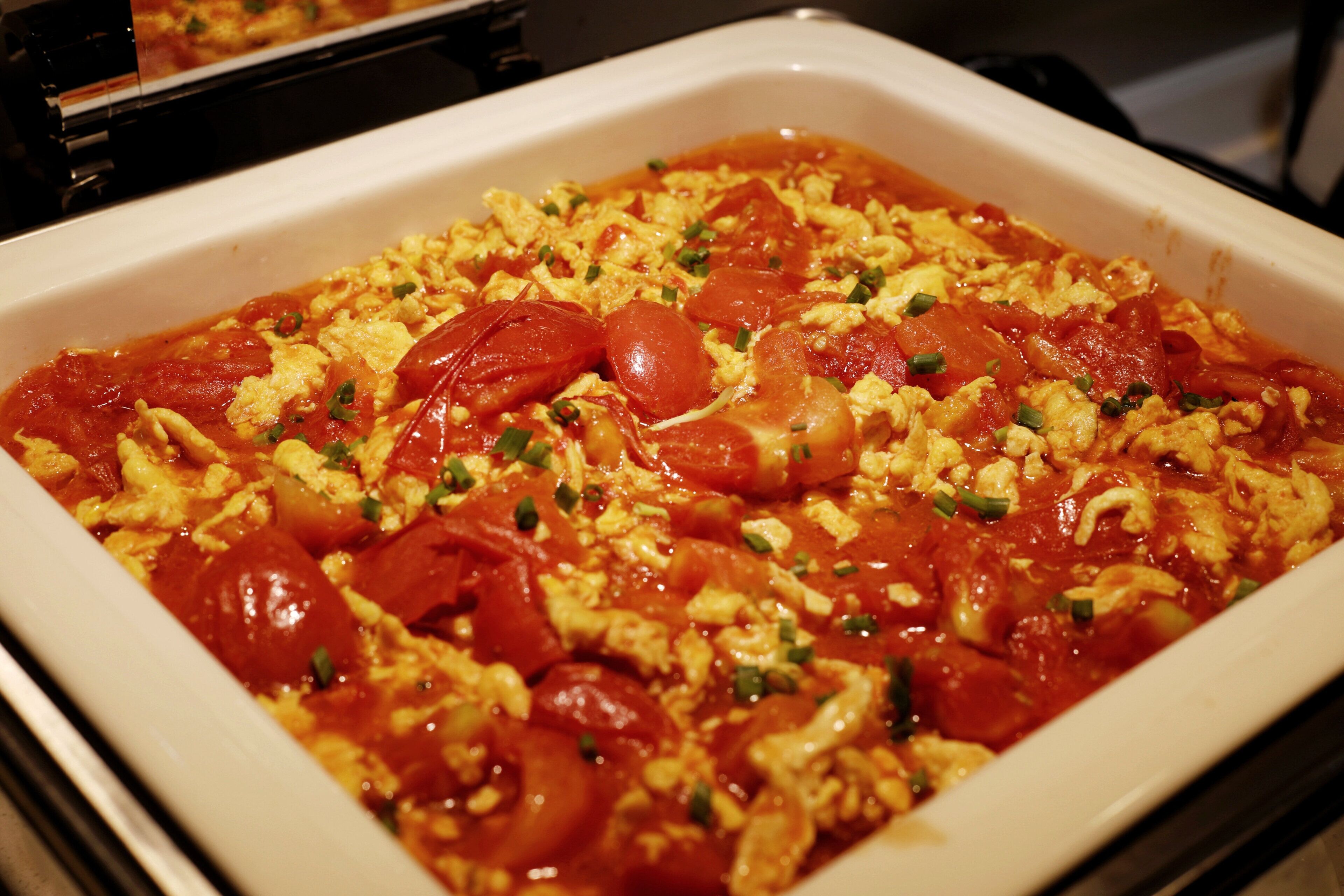 A white rectangular baking dish filled with scrambled eggs, tomatoes, and green onions.