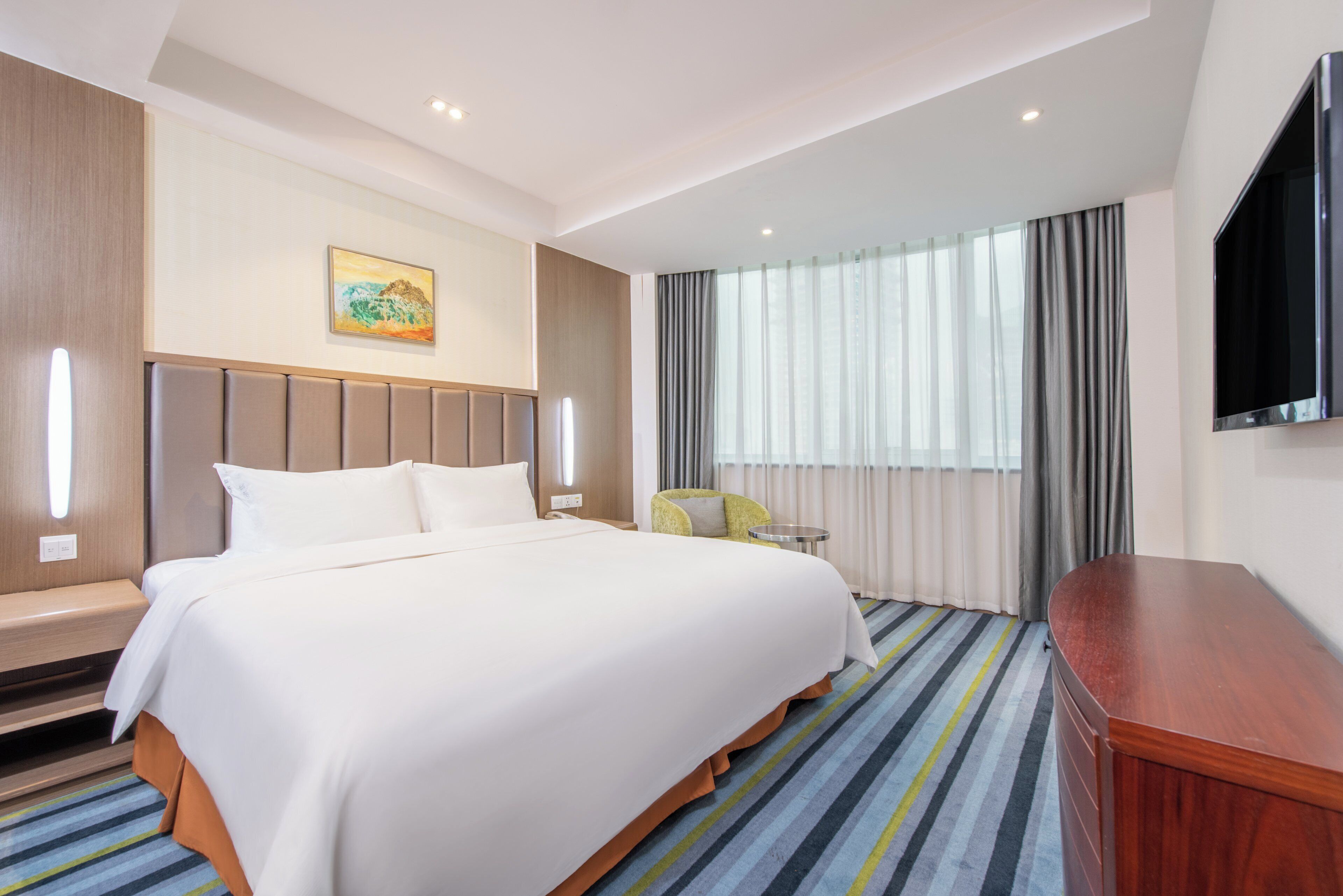 Habitació d'hotel amb un llit gran, escriptori, cadira, televisió i finestra amb cortines.
