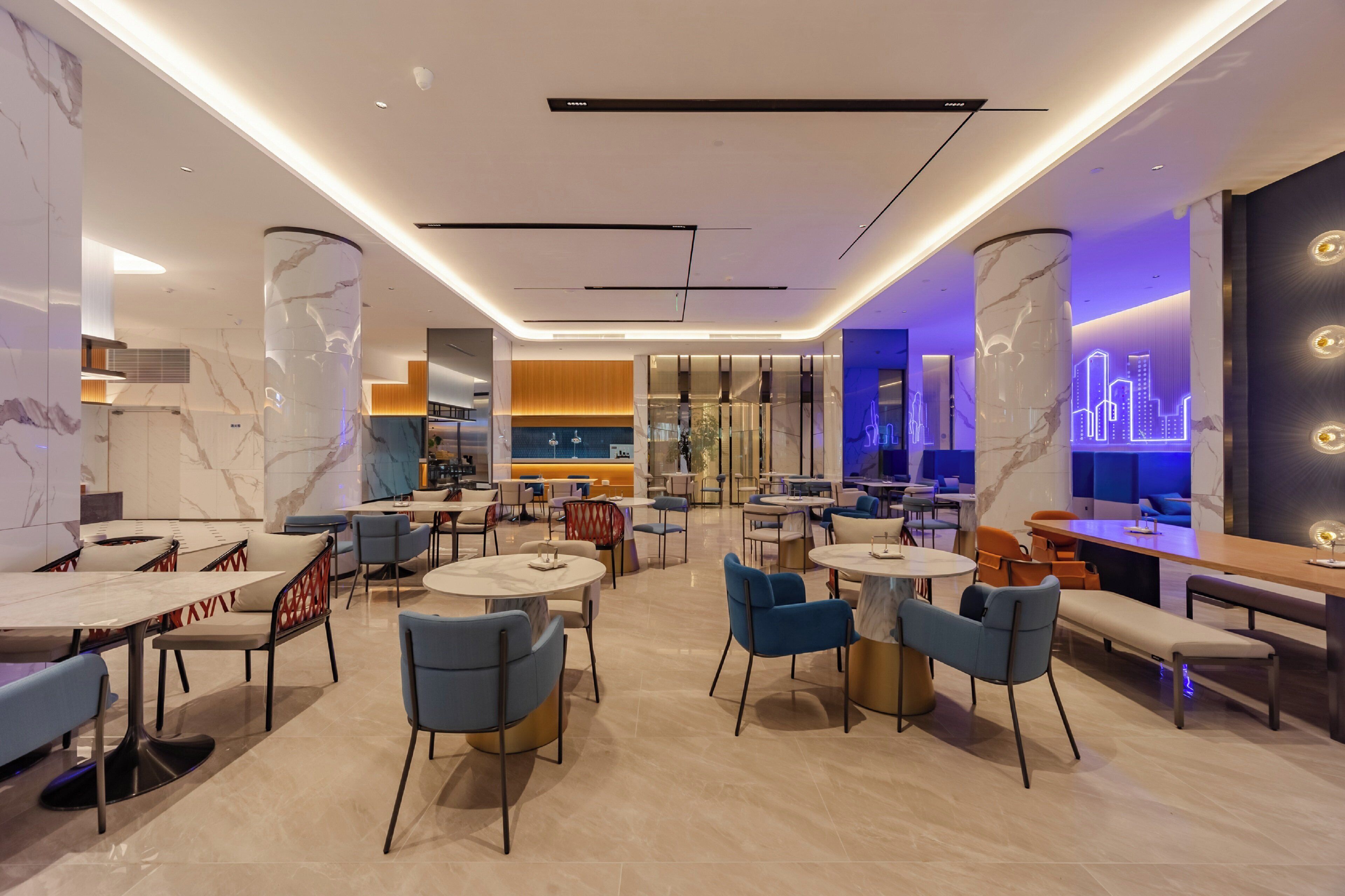A modern restaurant with marble columns, round tables, and blue chairs.