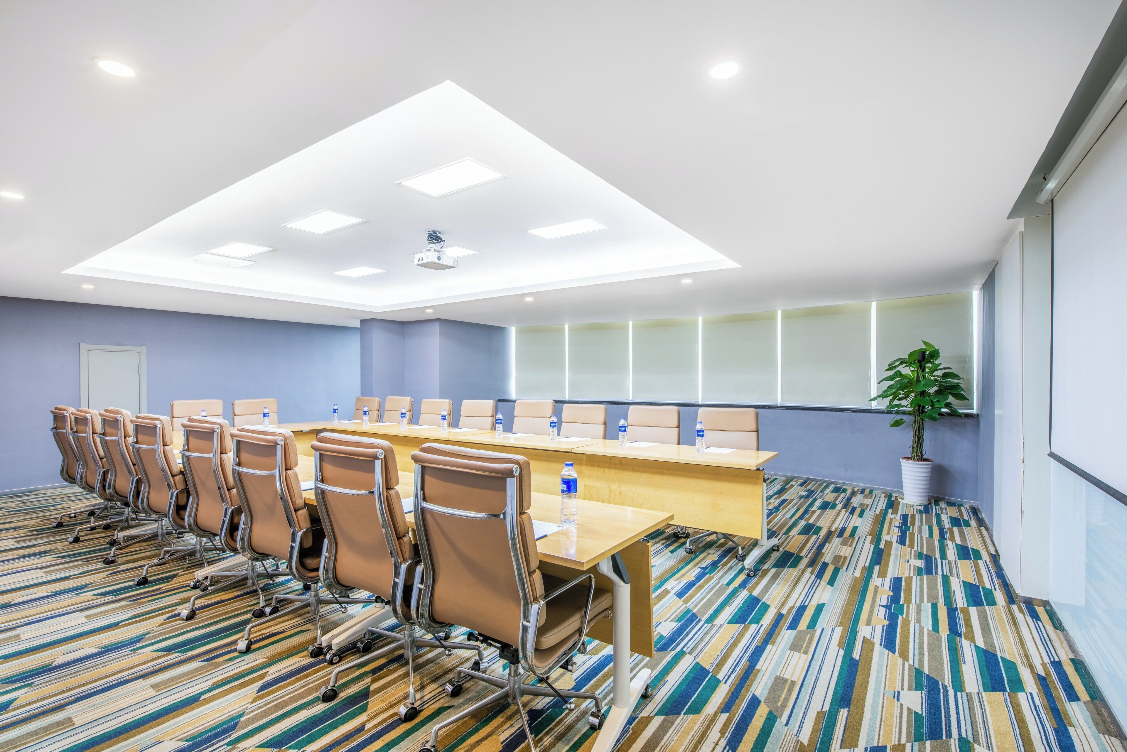 A conference room with a long table, chairs, a projector, and a potted plant.