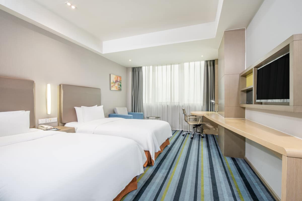 A hotel room with two beds, a desk, a chair, a TV, and a window with curtains.