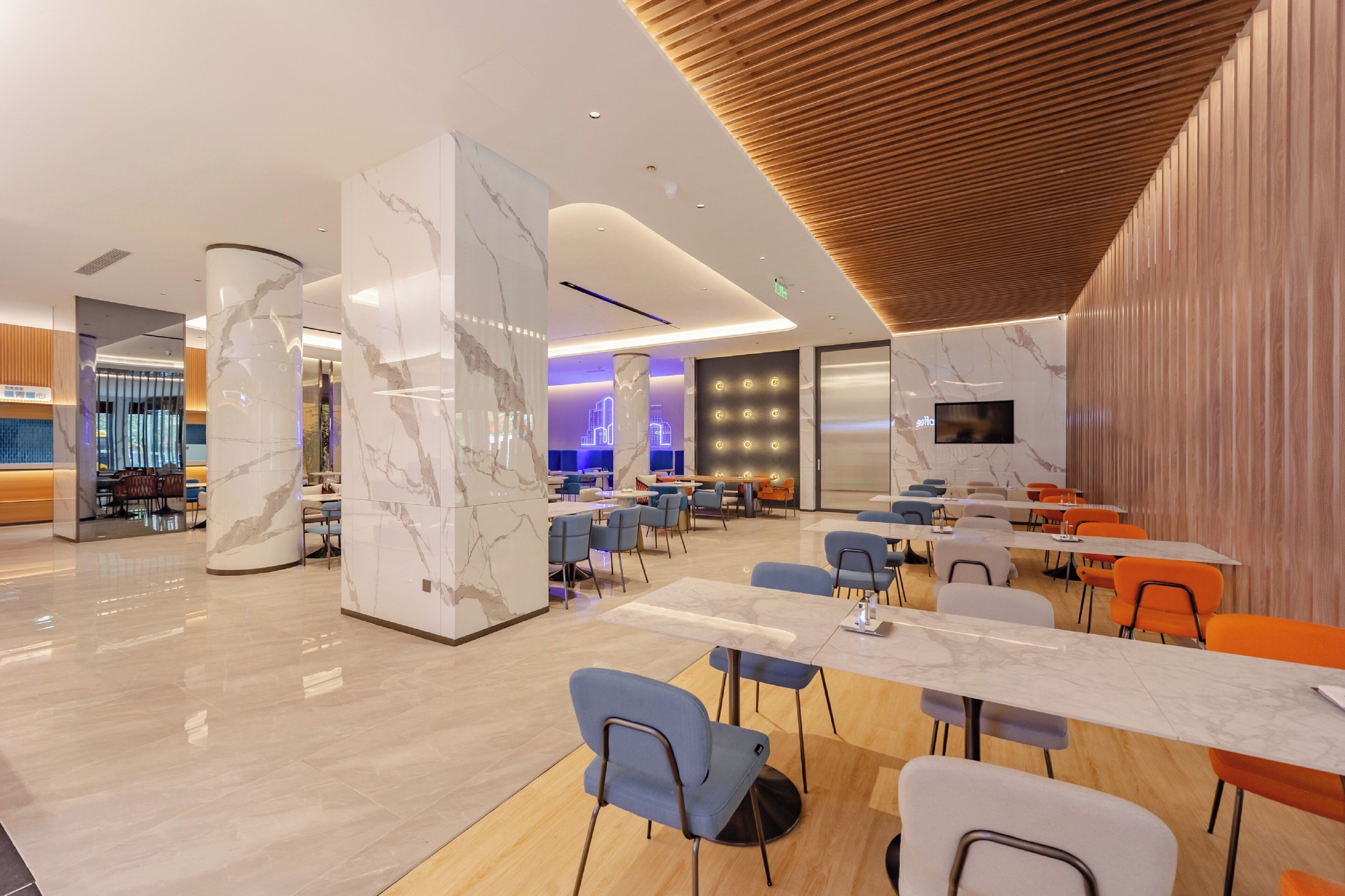 Un moderno vestíbulo de hotel con columnas de mármol, paneles de madera y diversas opciones de asientos, incluyendo mesas y sillas.