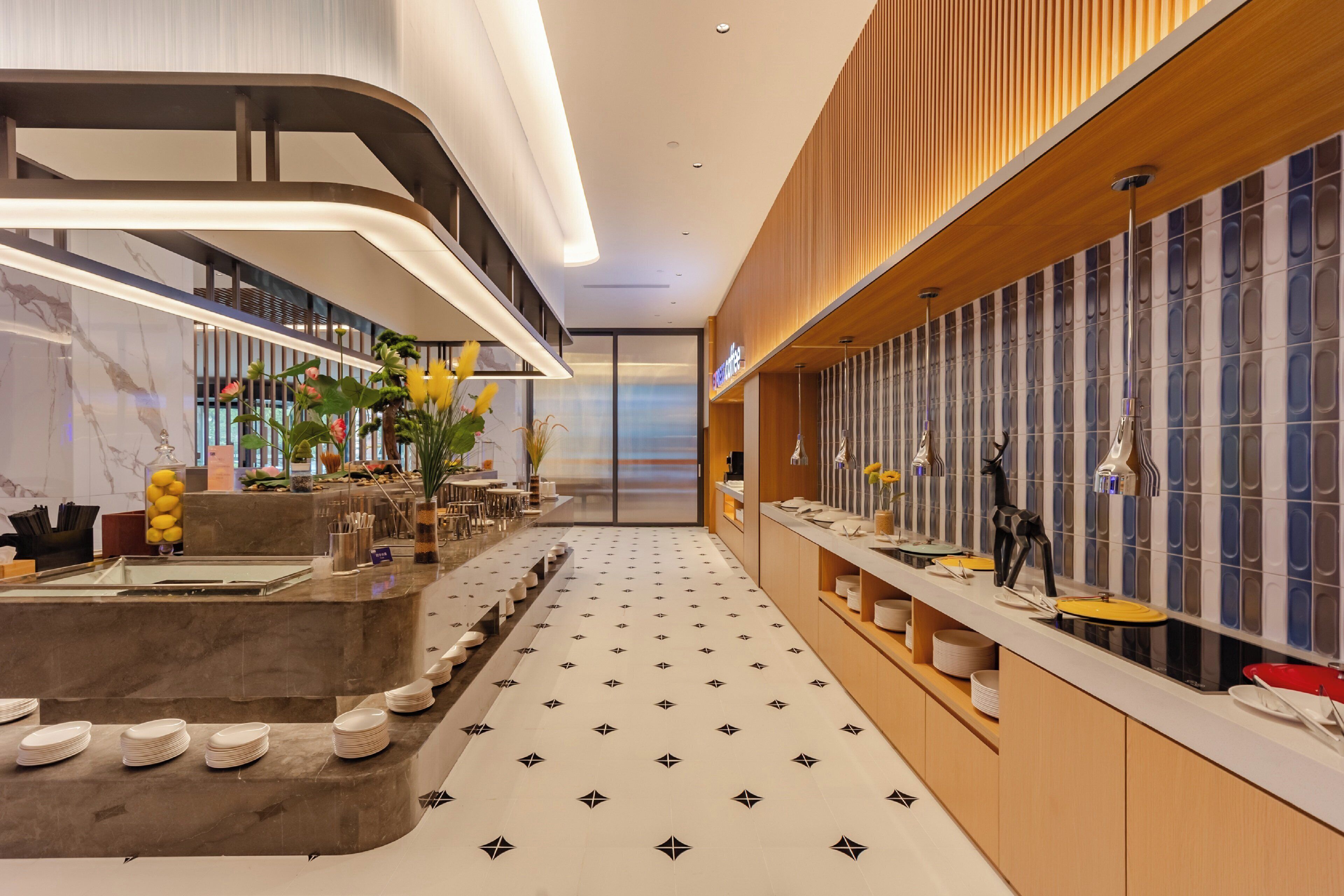 A modern hotel lobby with a marble reception desk, a long counter with various amenities, and a patterned floor.