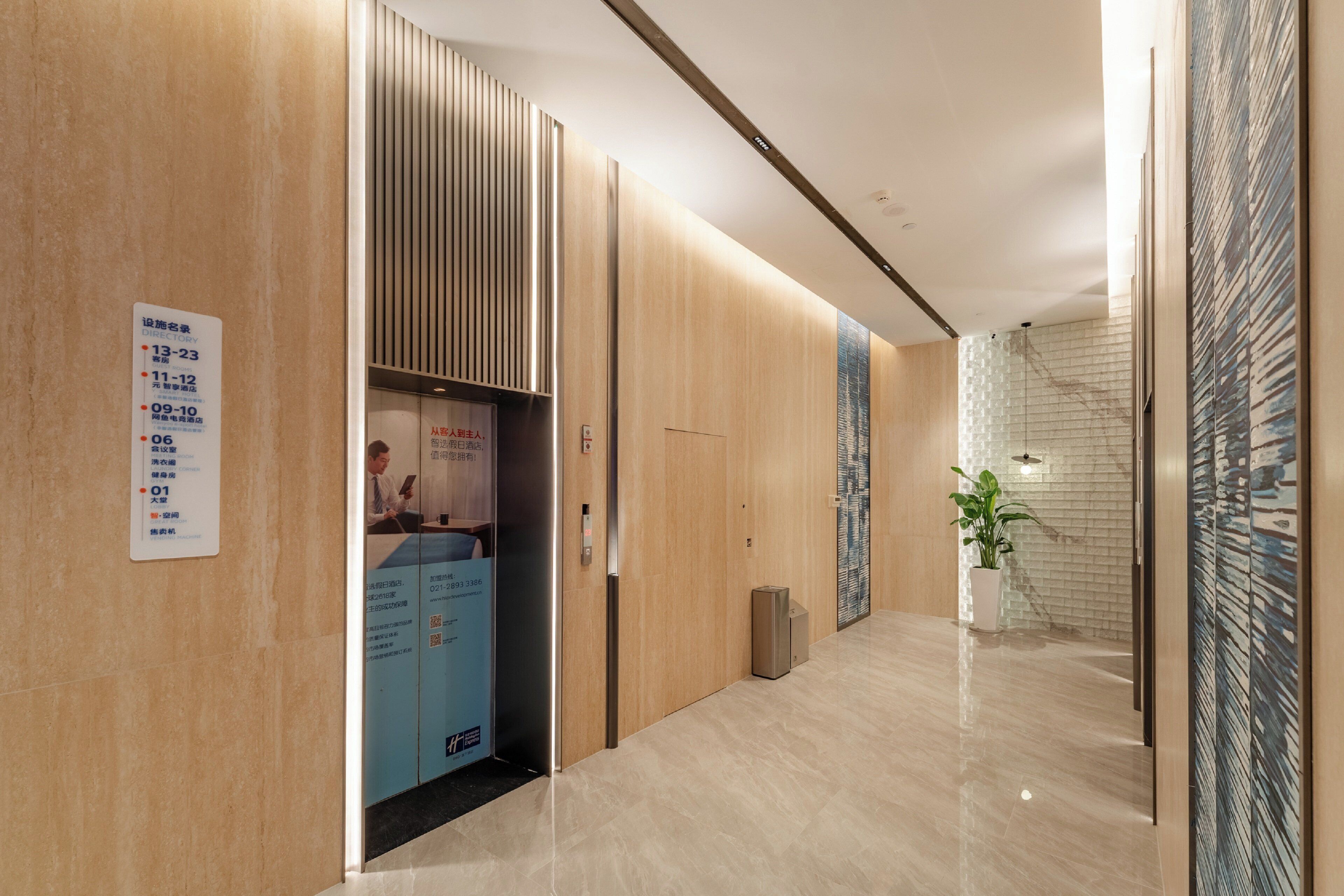 A modern hotel lobby with a wooden reception desk, a digital information board, and a potted plant.