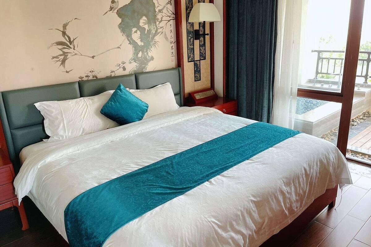 A neatly made bed with a white and teal bedspread, a teal pillow, and a wall with a floral mural.