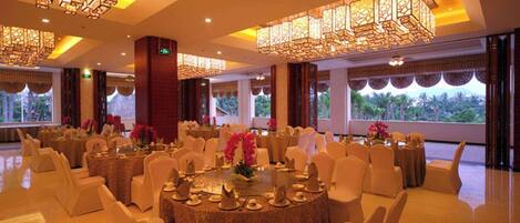 Un salón de banquetes con mesas redondas, sillas blancas e iluminación decorativa.