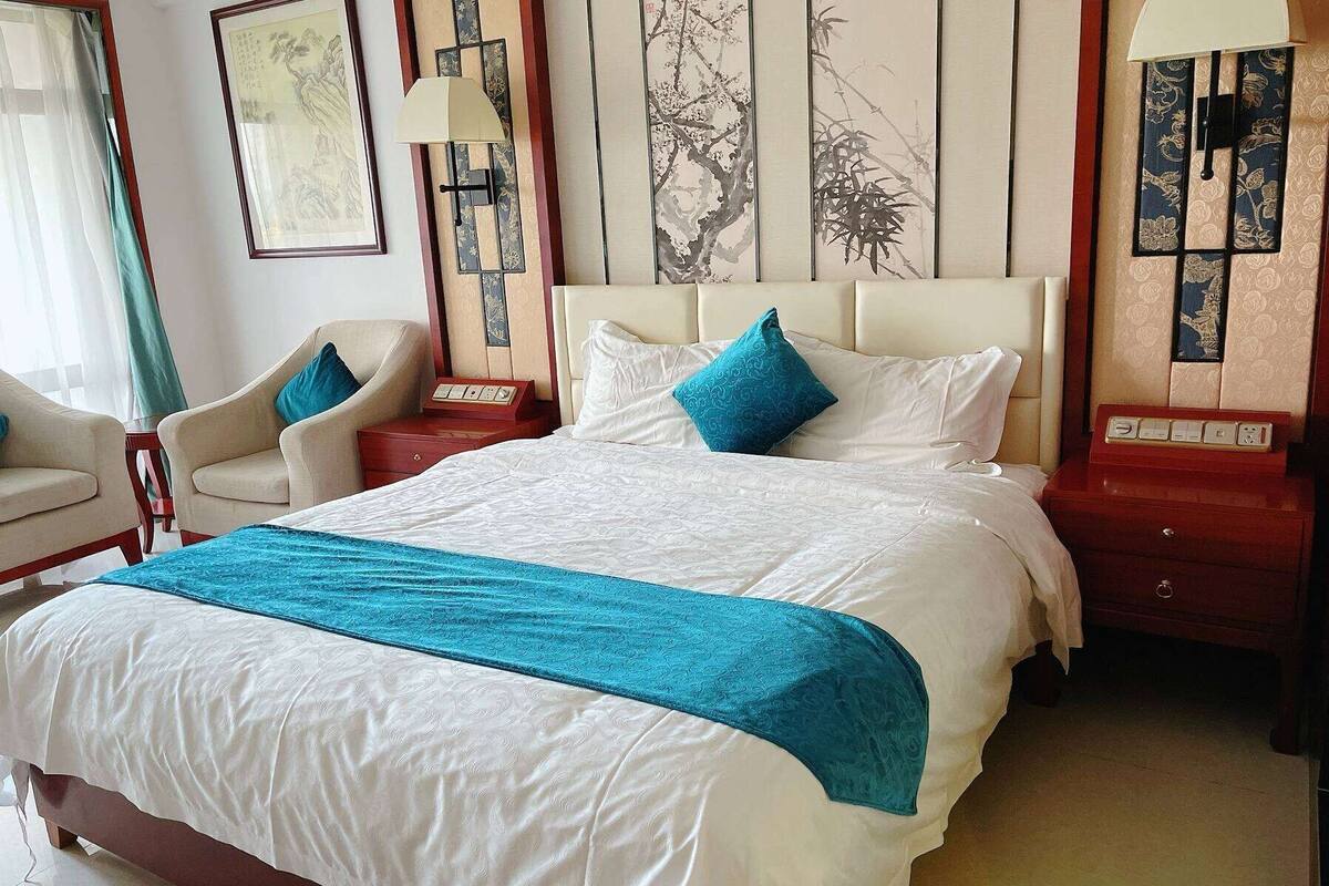 A hotel room with a large bed, two bedside tables, a chair, and artwork on the walls.