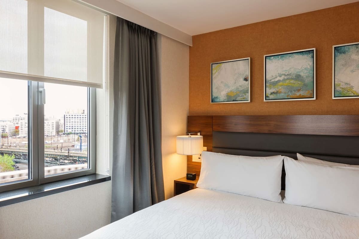 A hotel room with a large bed, a nightstand with a lamp, and three abstract paintings on the wall.