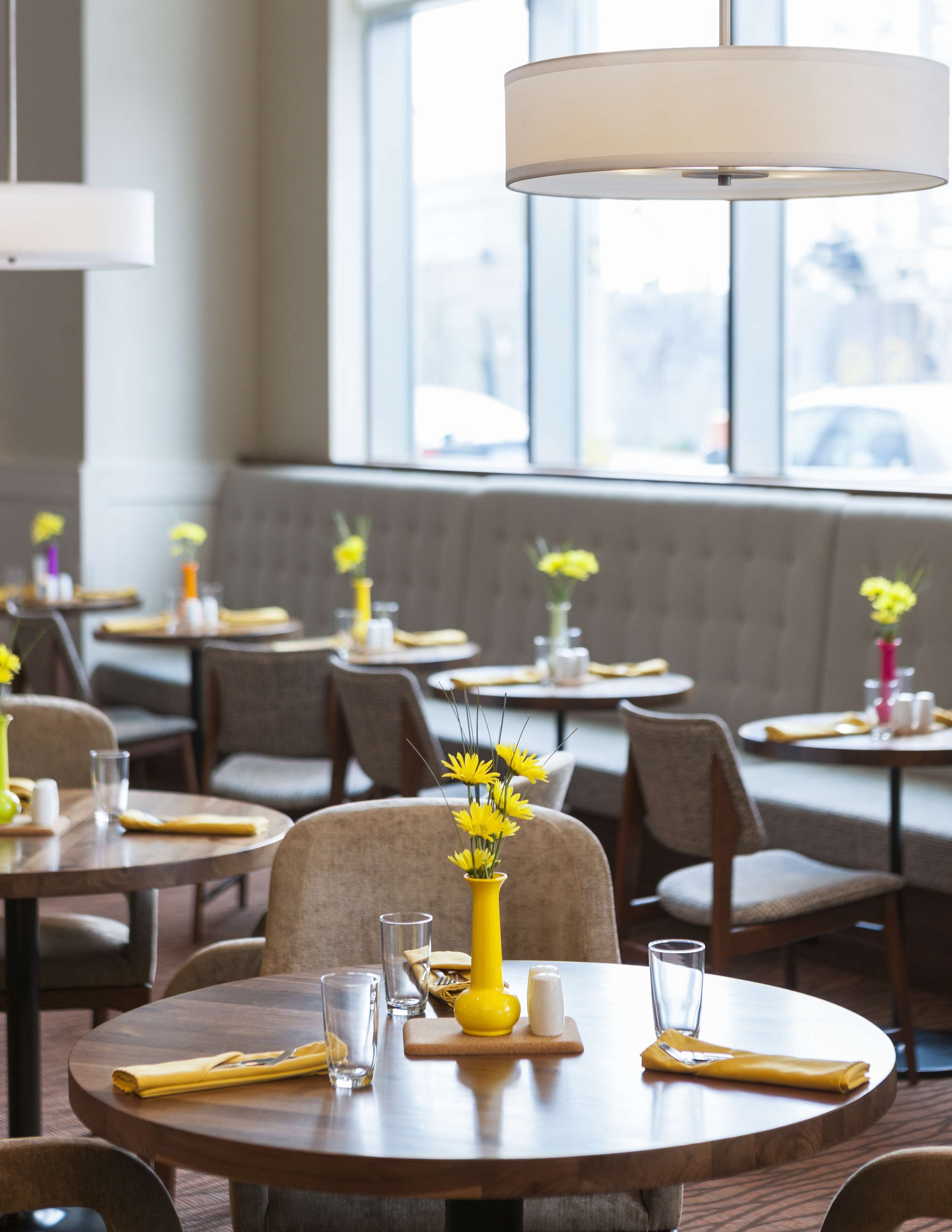 A restaurant with round tables, yellow napkins, and vases of yellow flowers.