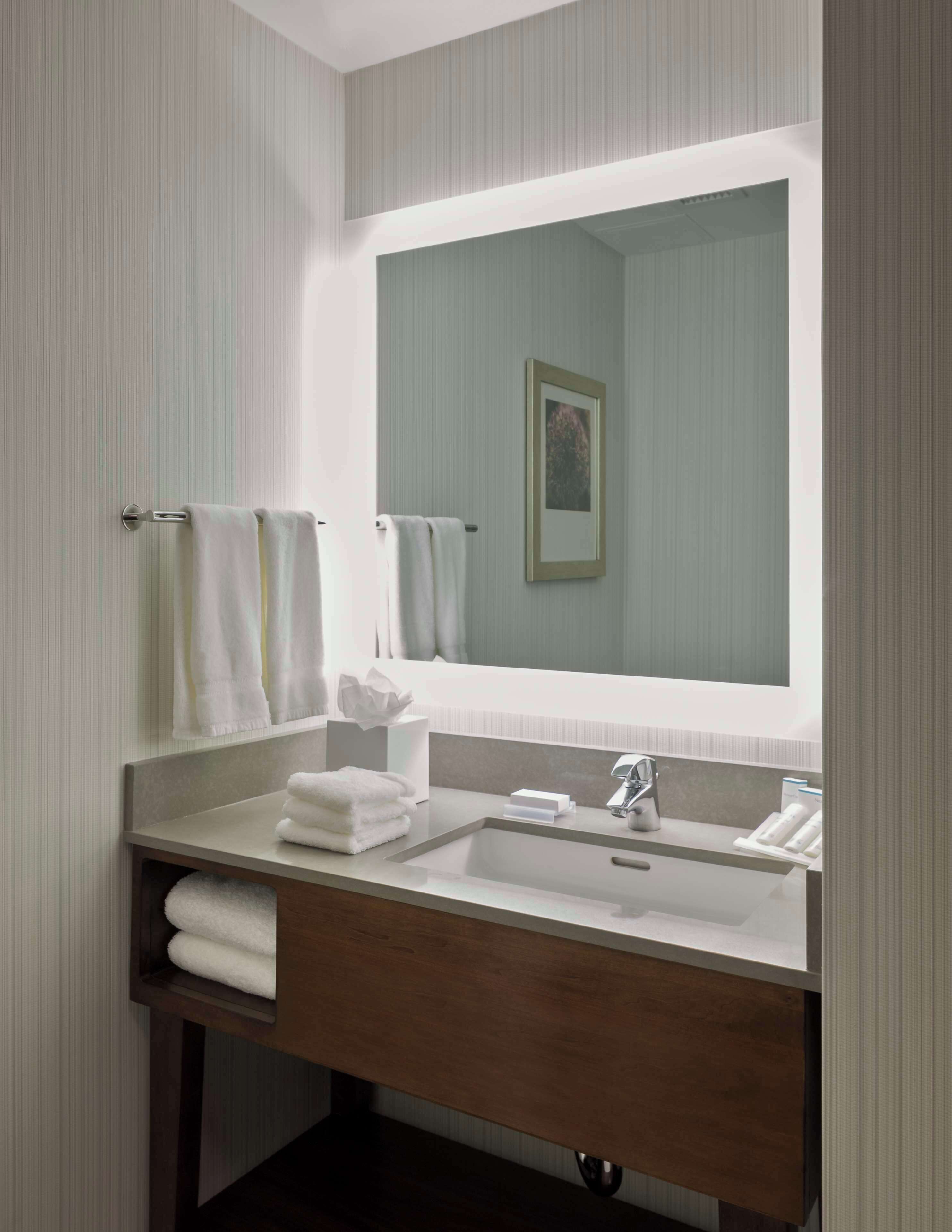 A modern bathroom with a large mirror, a sink, and two towel racks.