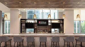 Zona de bar con un minibar, taburetes y un televisor mostrando el logotipo de Hilton Garden Inn.