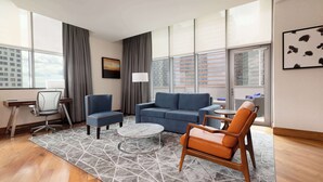 Una habitación de hotel moderna con un sofá azul, un sillón naranja, una mesa de centro redonda y un escritorio con una silla.