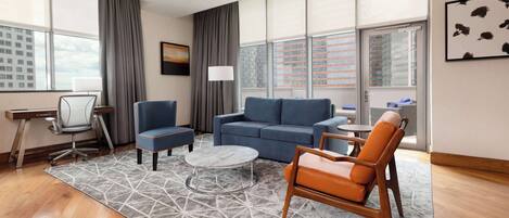 Una habitación de hotel moderna con un sofá azul, un sillón naranja, una mesa de centro redonda y un escritorio con una silla.