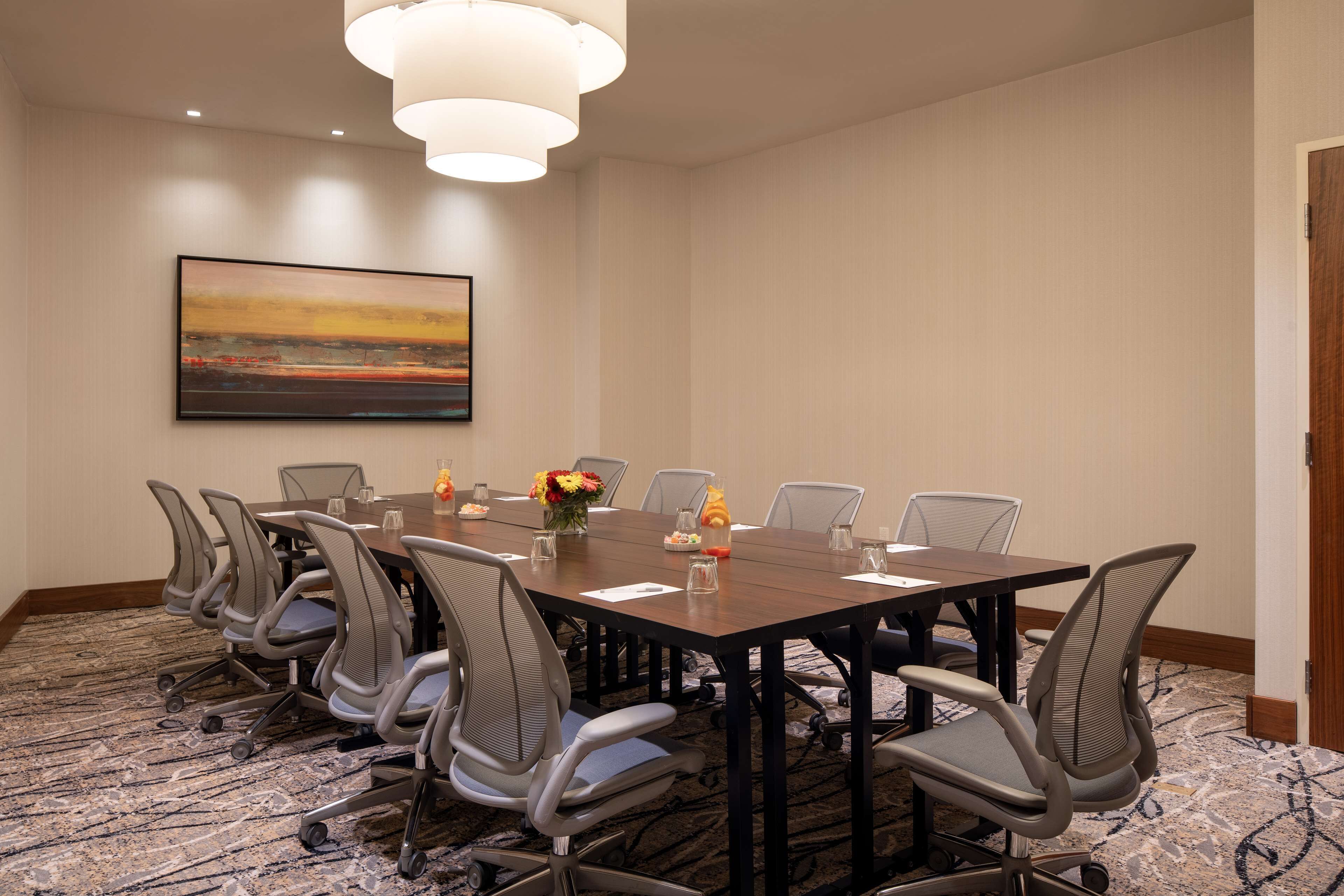 A conference room with a long table, chairs, a painting, and a carpeted floor.