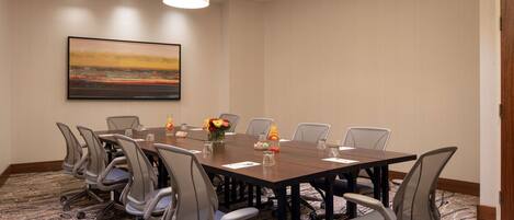 A conference room with a long table, chairs, a painting, and a carpeted floor.