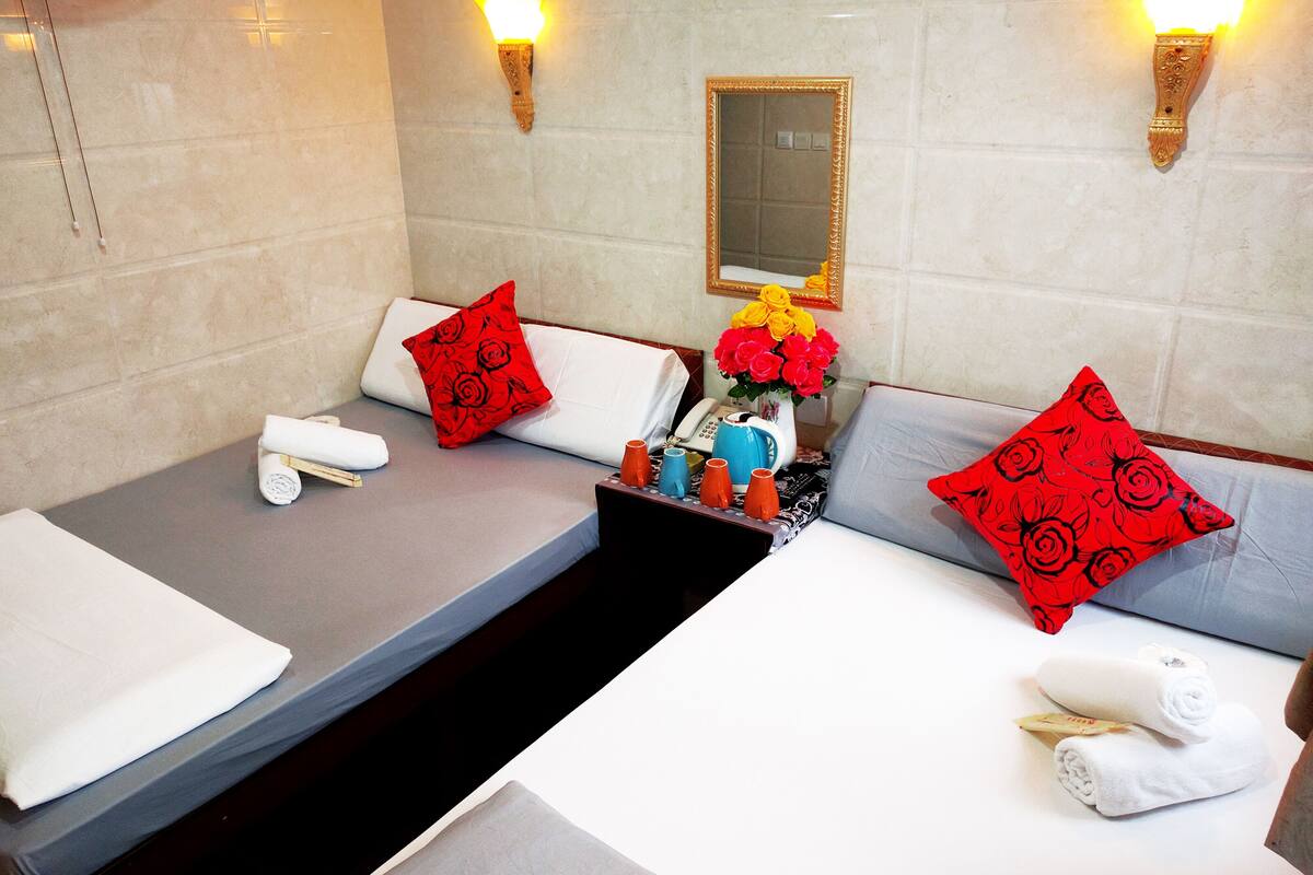 A hotel room with two beds, each with a pillow, a small table with toiletries, and a vase of flowers.